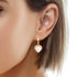 A close-up shot showcases a person's ear wearing the Heart Shaped Zirconia Stones Dangle Earrings, made with 14k gold filled material. The large heart-shaped zirconia gemstone stands out, accentuated by the individual's short cropped hair and smooth skin, highlighting the elegance of this radiant jewelry piece.